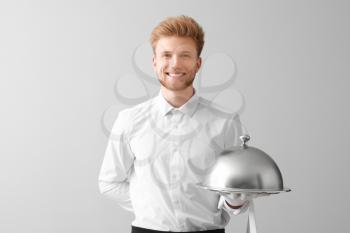Handsome waiter with tray and cloche on light background�
