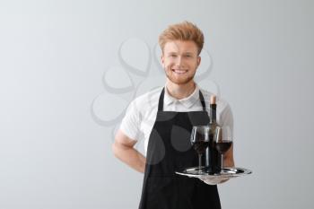 Handsome waiter with wine on light background�