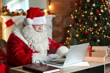 Santa Claus with laptop in room decorated for Christmas�