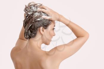 Beautiful young woman washing hair against light color background�