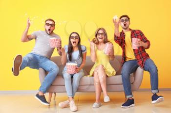 Emotional friends with popcorn watching movie on sofa near color wall�