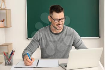 Handsome male teacher checking homework in classroom�