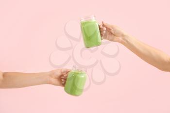 Female hands with tasty green smoothie in mason jars on color background�