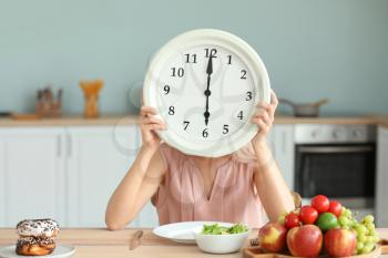 Woman with clock and food sitting in kitchen. Diet concept 