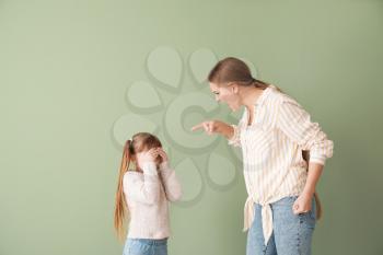 Angry mother scolding her little daughter on color background�