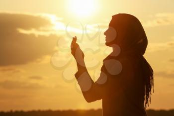 Beautiful Muslim woman praying outdoors at sunset�