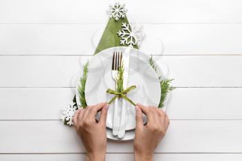 Female hands and beautiful table setting for Christmas dinner on white wooden background�