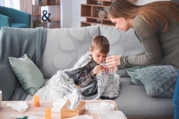 Mother giving medicine to her son ill with flu at home�