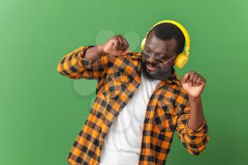 Handsome African-American man listening to music and dancing against color background�