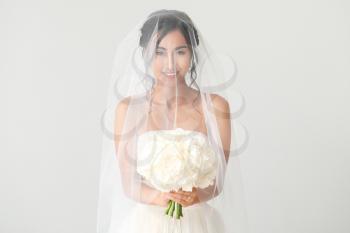 Beautiful young Asian bride on light background�