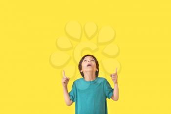 Surprised little boy pointing at something on color background�