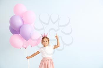 Little girl with balloons and raised index finger on color background�