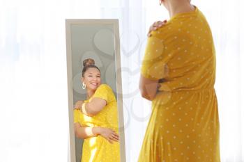 Young body positive woman looking in mirror at home�