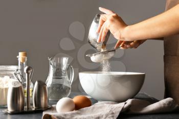 Woman sieving flour in kitchen�