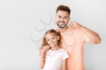 Portrait of man and his little daughter brushing teeth on light background�