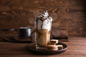 Glass of tasty frappe coffee with sweets on wooden table�