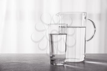 Glass and jug of fresh water on table indoors�