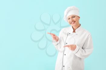 Beautiful female chef pointing at something on light background�