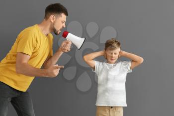 Little boy ignoring his angry father with megaphone against grey background�