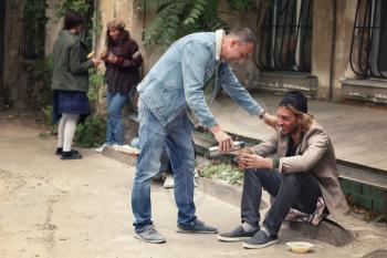Volunteer giving drink to homeless man outdoors�