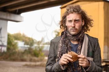 Portrait of poor homeless man with piece of bread outdoors�
