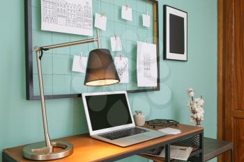 Comfortable workplace with mood board and laptop near color wall�