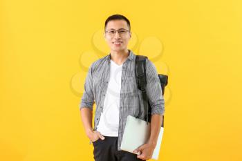 Male Asian student with laptop on color background�