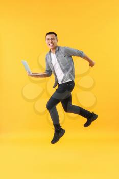 Happy jumping Asian programmer with laptop on color background�