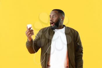 Emotional African-American man listening to music on color background�