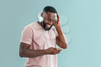 African-American man listening to music on color background�