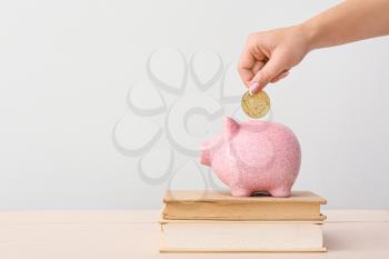 Female hand with coin, piggy bank and books on light background�