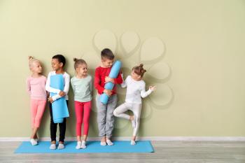 Little children with yoga mats near color wall in gym�