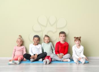 Little children with yoga mats sitting near color wall in gym�