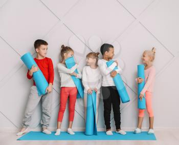 Little children with yoga mats near grey wall in gym�