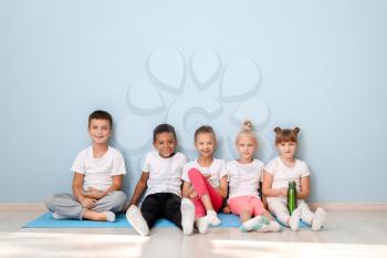 Little children with yoga mats sitting near wall in gym�