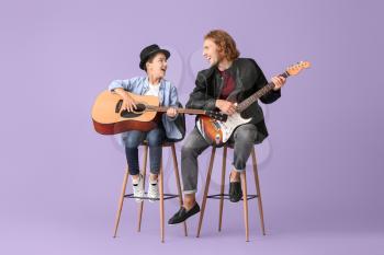Man and his little son playing guitars on color background�