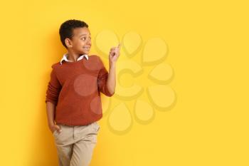 Fashionable African-American boy in autumn clothes pointing at something on color background�