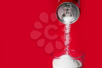 Pouring of sugar from can into glass on color background�