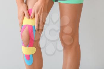 Sporty woman with physio tape applied on knee against light background, closeup�