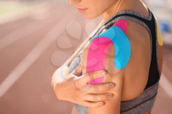 Sporty woman with physio tape applied on shoulder at stadium, closeup�