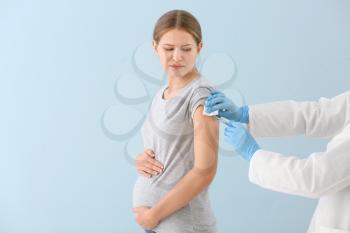 Doctor vaccinating pregnant woman on color background�
