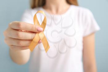 Young woman with golden ribbon on grey background, closeup. Cancer awareness concept�