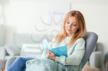 Beautiful mature woman reading book at home 