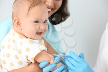 Pediatrician vaccinating little baby on light background�