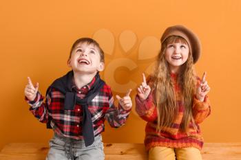 Cute little children in autumn clothes pointing at something while sitting near color wall�