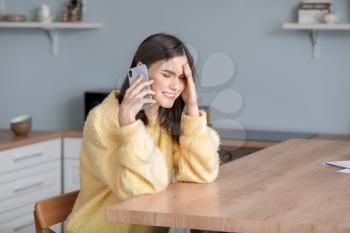 Worried young woman talking by phone at home�