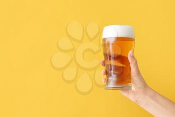 Hand with glass of beer on color background�