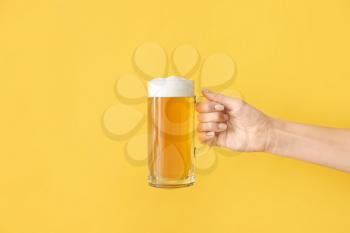Hand with mug of beer on color background�