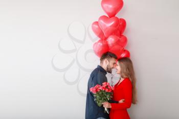 Happy young couple with heart-shaped balloons and flowers on light background. Valentine's Day celebration�