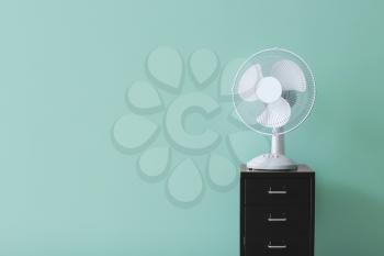 Electric fan on chest of drawers near color wall�